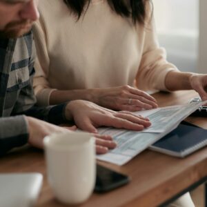 A man and woman reviewing financial papers at a wooden table with a keyboard and coffee mug.